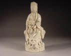 A 17th C Dehua figure of Guanyin seated on a rockwork holding a child